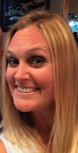 Smiling woman with long blonde hair poses for a close-up selfie, showcasing her cheerful expression and bright eyes in a casual setting.